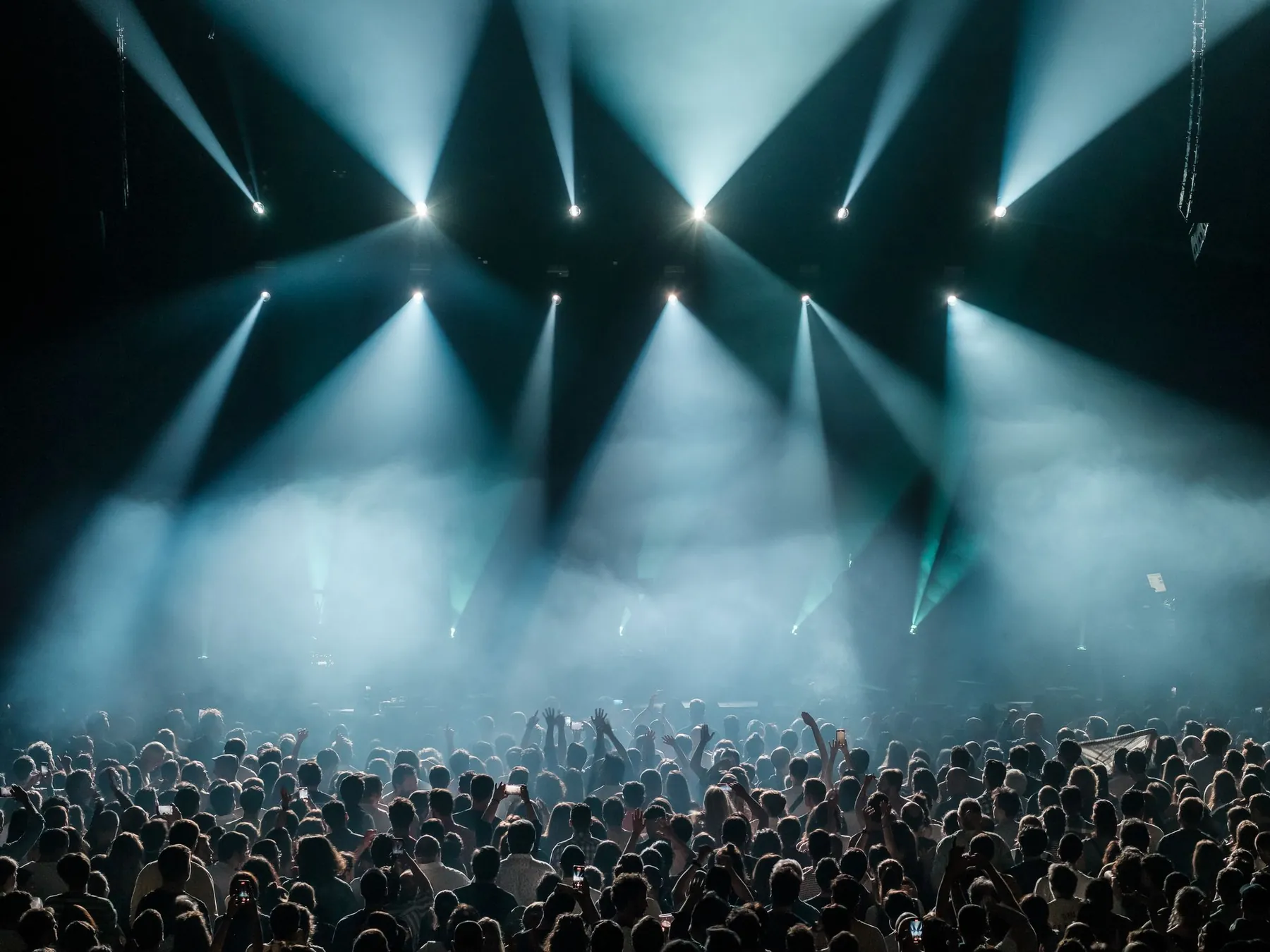 A crowd under teal stage light beams and haze.
