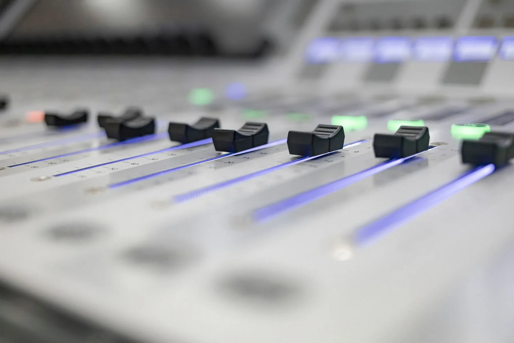 Faders on a white mixing console, their tracks lit in blue.