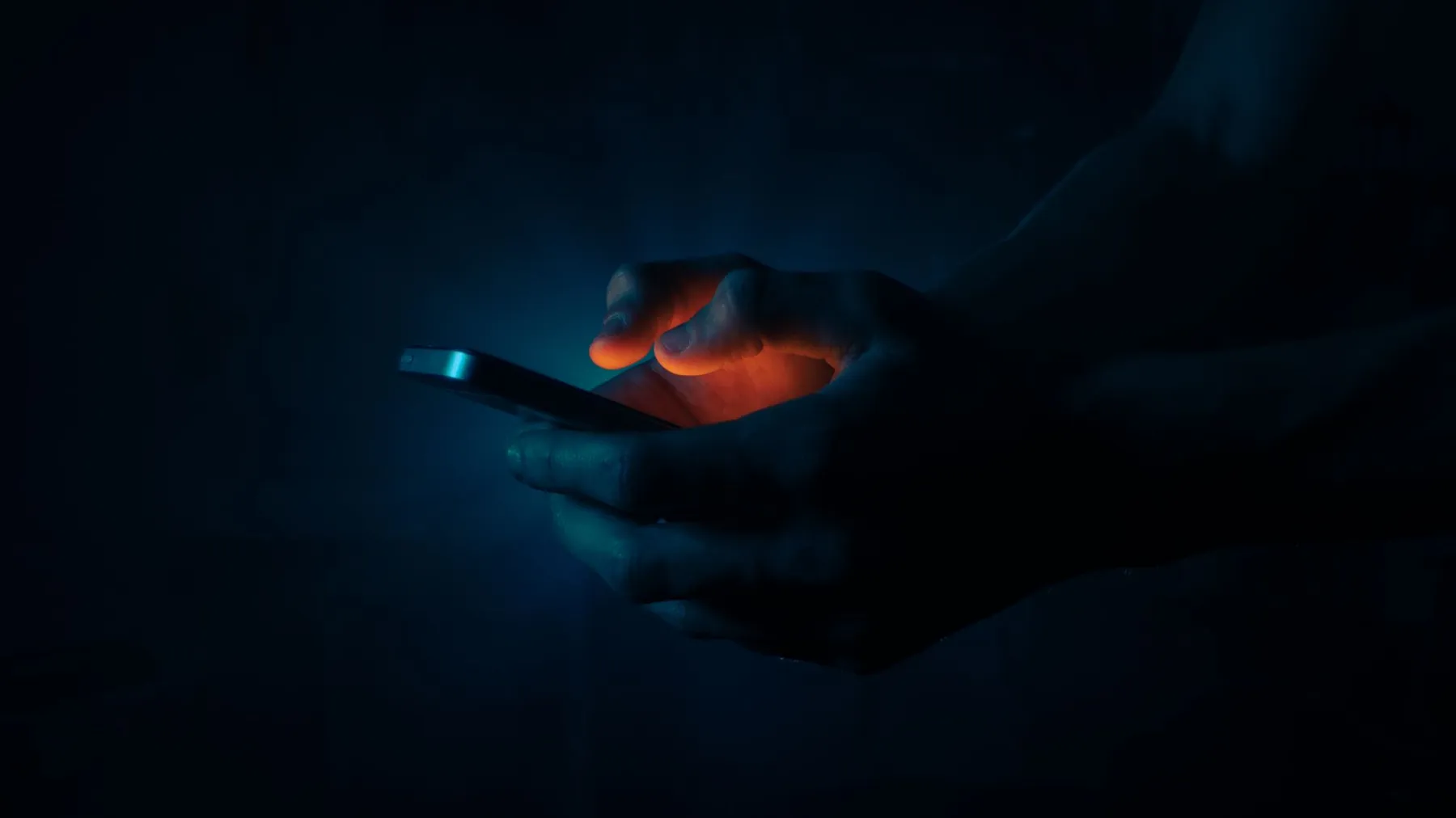 Hands holding a phone in the dark, lit by its screen.