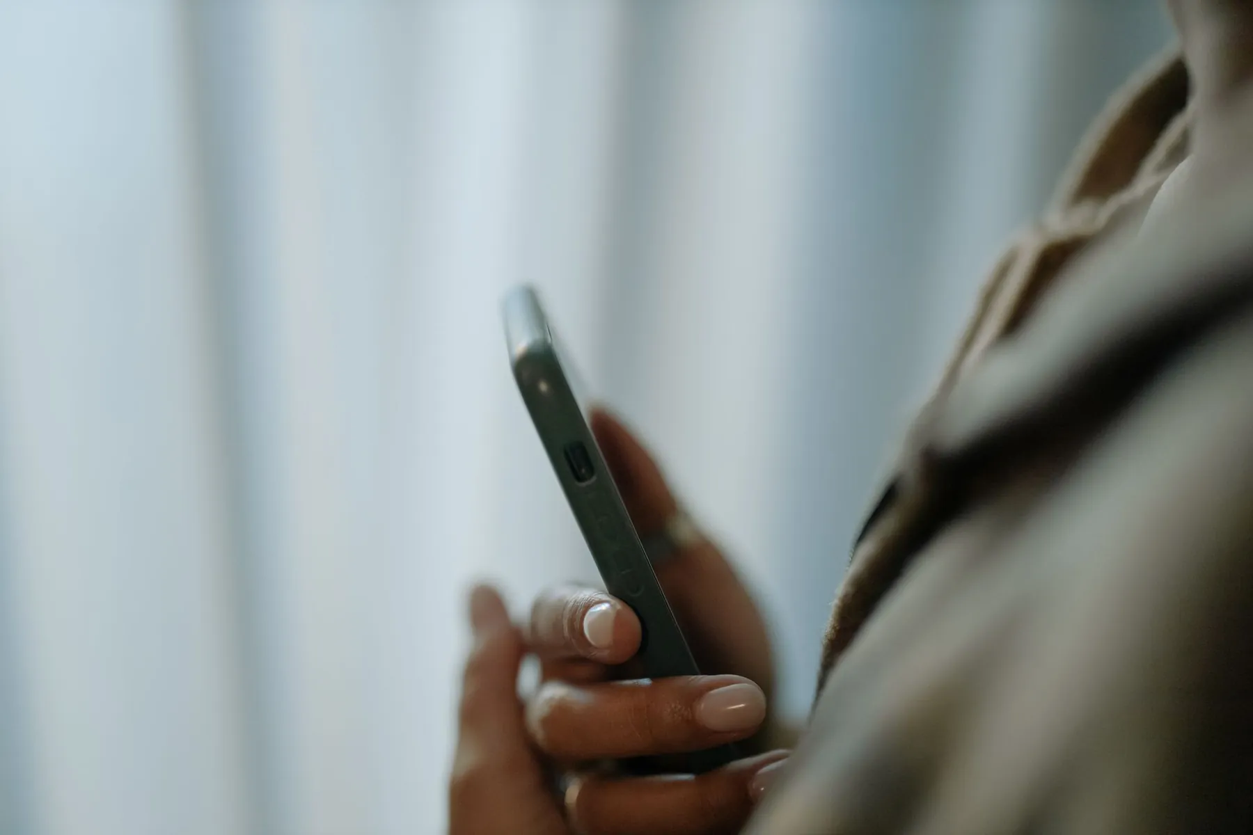 A hand holding a phone against a soft, pale background.