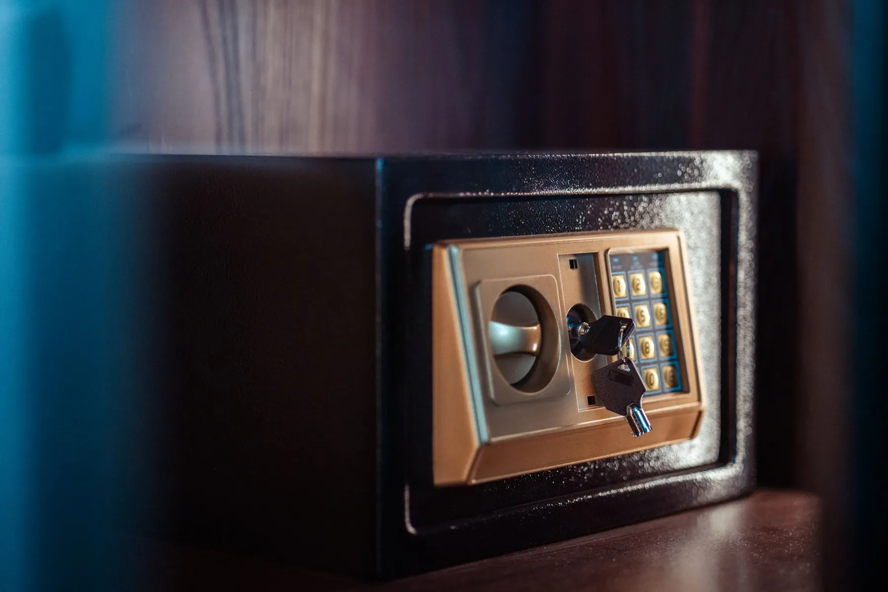 A small safe with a keypad and a key in its lock.