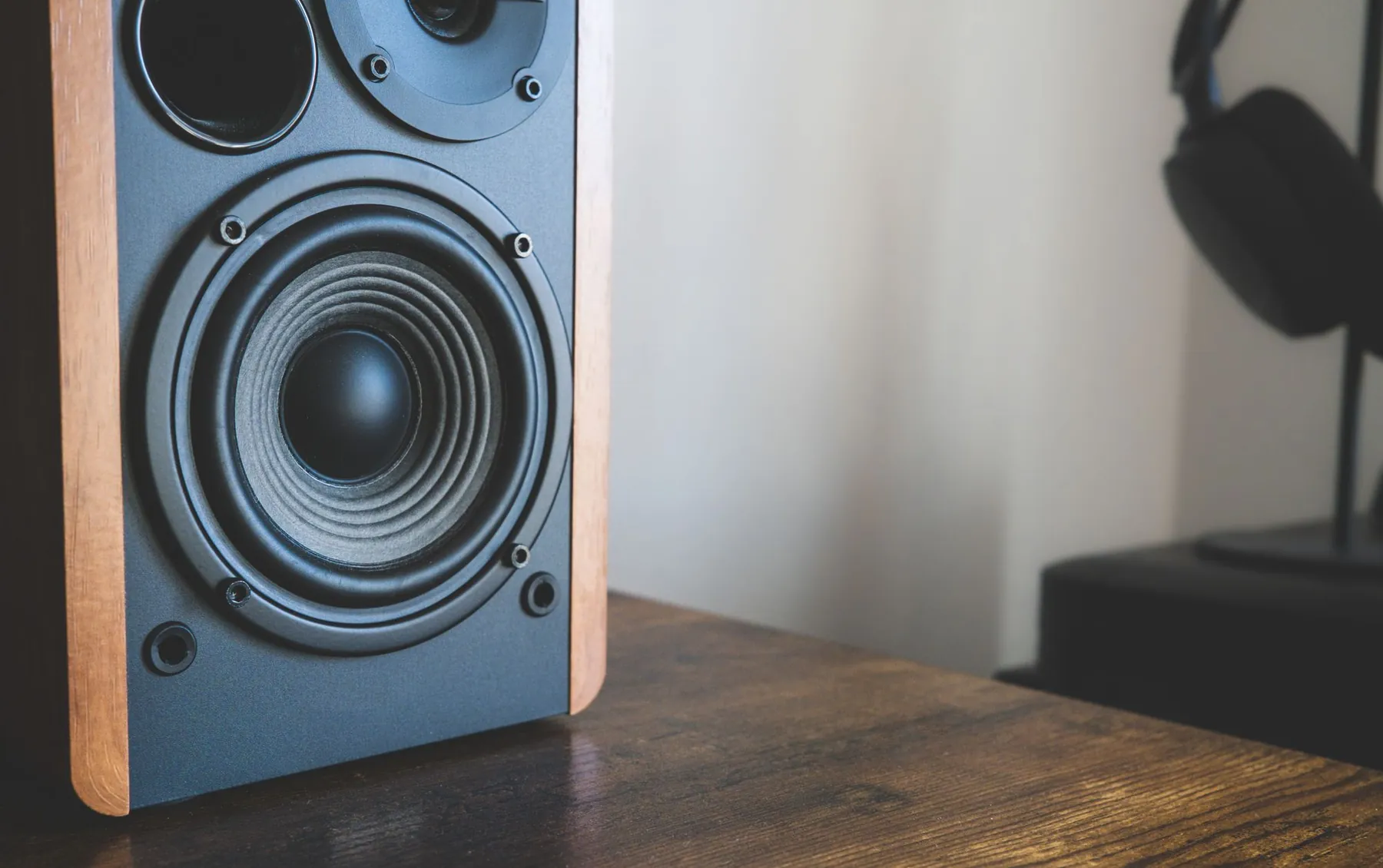 A speaker on a wooden desk, headphones on a stand behind it.