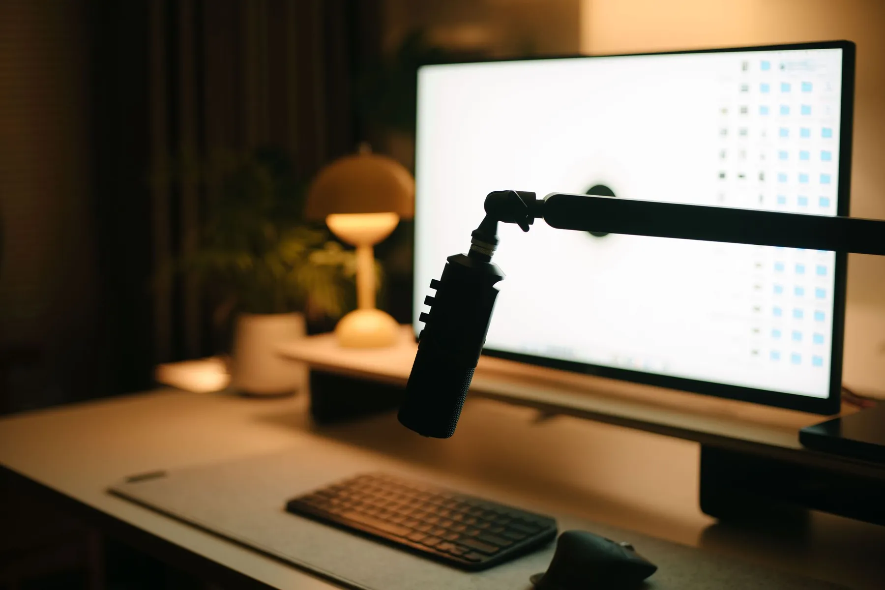 A desk with a microphone on an arm, a glowing screen and a warm lamp.